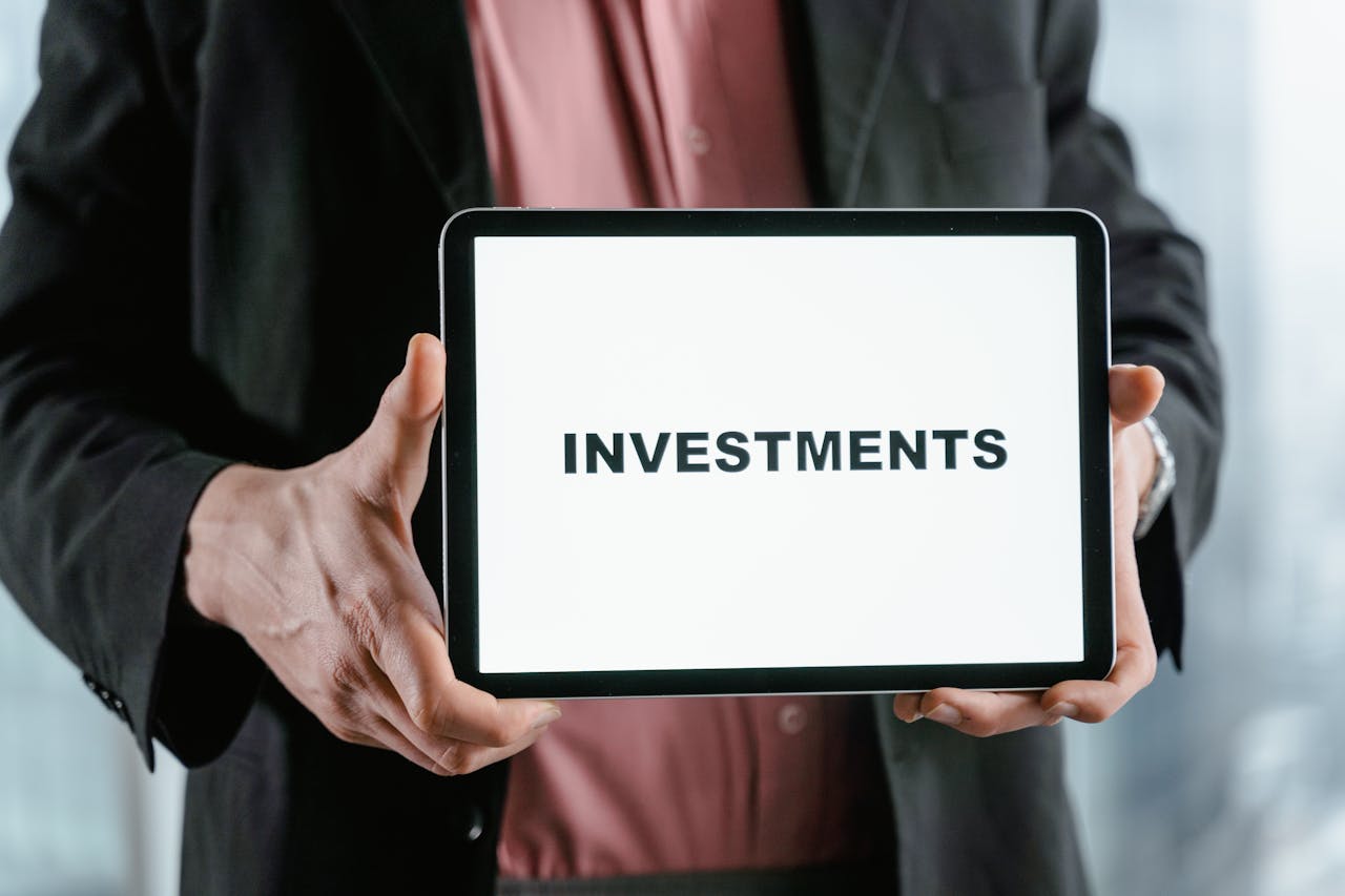 A businessman in a suit holds a tablet displaying the text INVESTMENTS.
